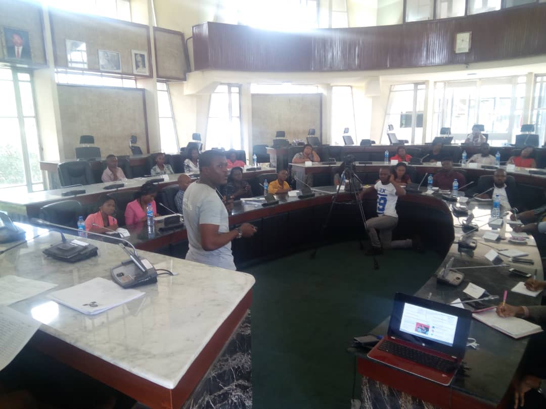 Adebayo Chike teaching in a council chamber, attendees around the curved desks