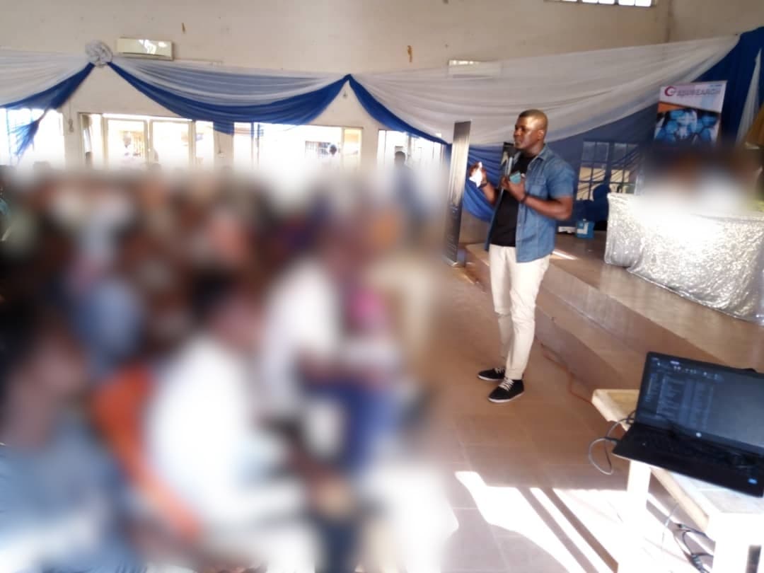 Adebayo Chike leading a session in a packed hall, audience blurred for privacy